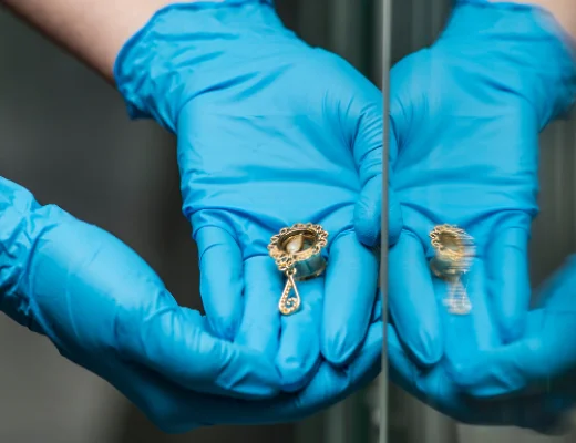 Mains gantées bleues tenant un petit bijou doré près d’un miroir